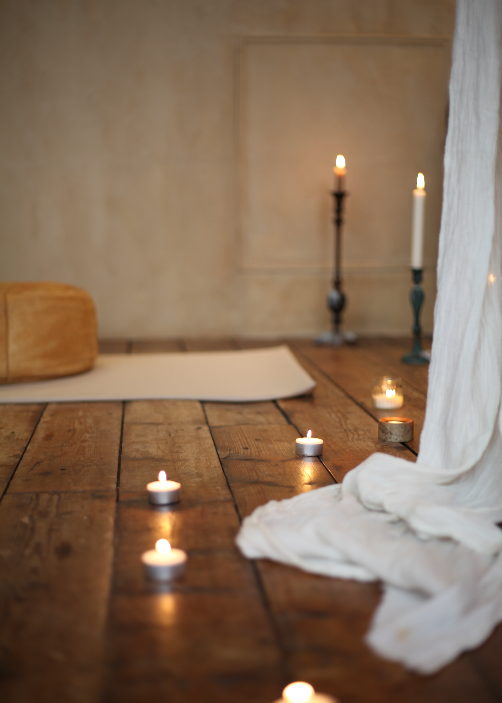 Sfeervolle meditatie- en ontspanningsruimte met kaarslicht, yogamat en kussens op een rustieke houten vloer, perfect voor spirituele en intuïtieve sessies.