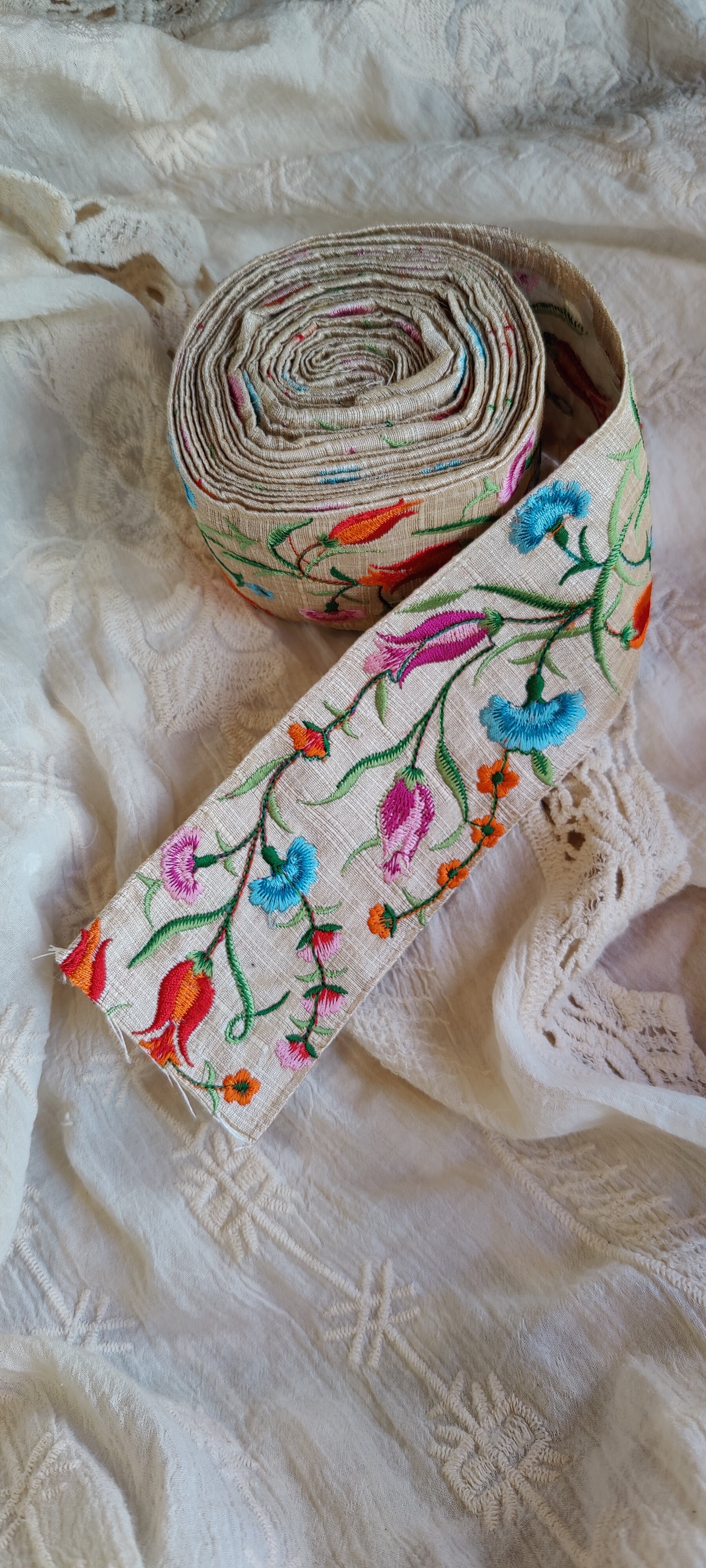 Roll of colorful embroidered fabric on a textured white background
