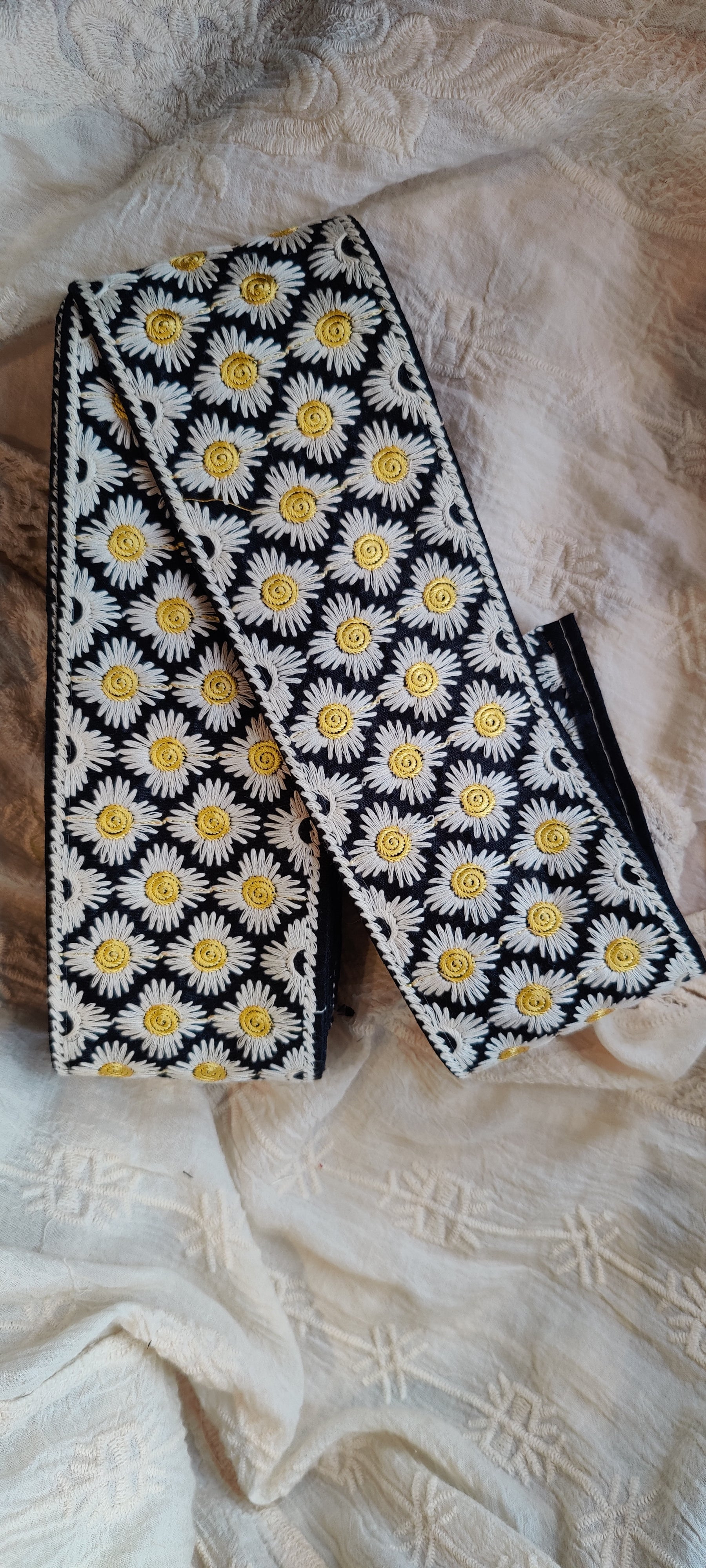 Black headband with white and yellow floral pattern on a textured fabric background